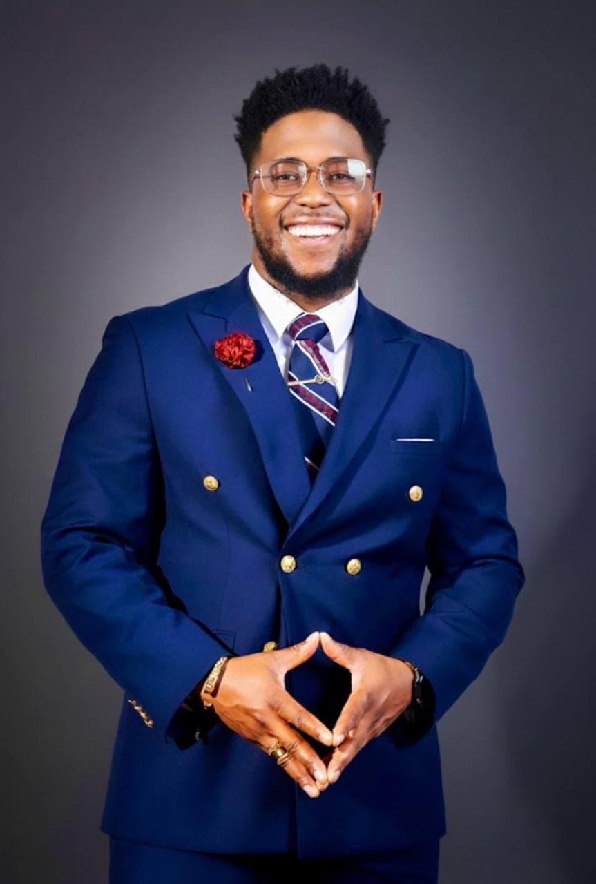 Dominic Fobi, co-founder of Keldya, photographed in a navy double-breasted suit with a red lapel pin and gold accents, smiling warmly
